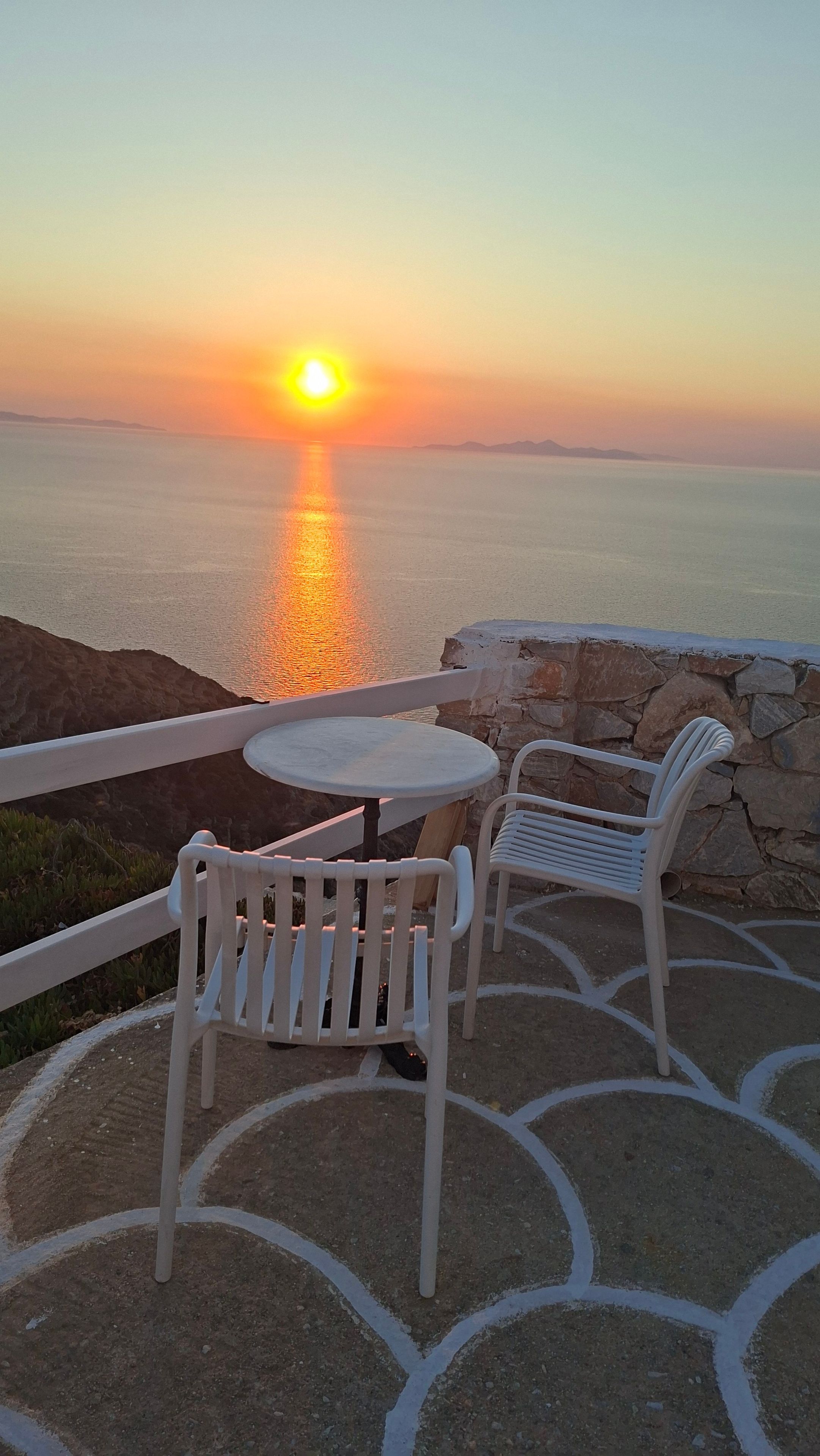 Vista al atardecer desde una terraza con mesa y sillas, con vista al mar.
