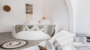 Habitación moderna y minimalista con zona de estar circular, cama con ropa de cama estampada y una lámpara de pared.