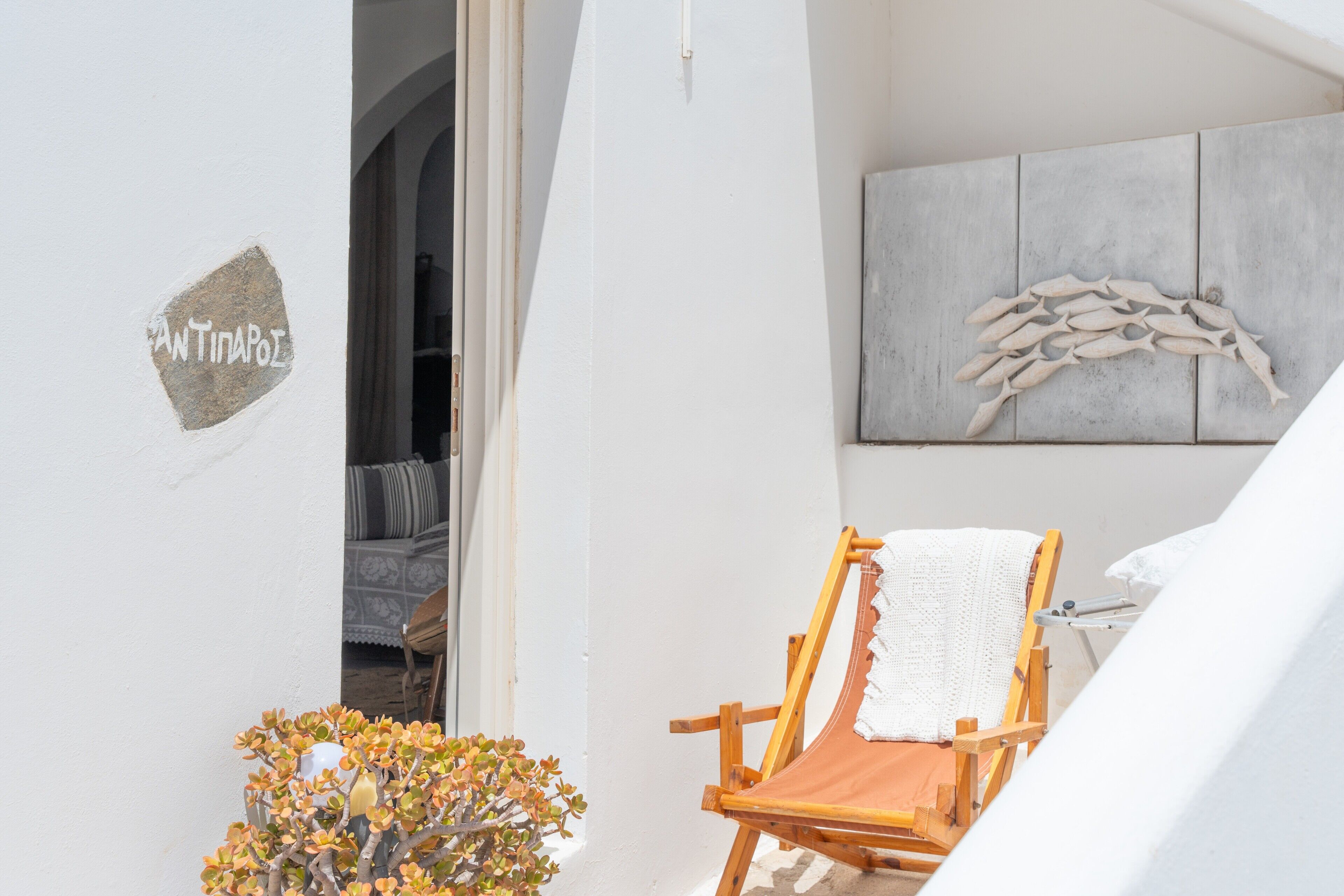 Un mur blanc orné d’une plaque de pierre, une chaise en bois avec une serviette blanche, et une œuvre d’art représentant des poissons, accrochée au mur.