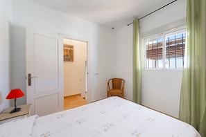 A bedroom with a bed, a chair, a door, a window with curtains, and a lamp on a nightstand.