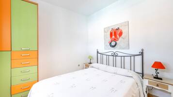 A bedroom with a bed, a nightstand, a lamp, a wardrobe, and a wall-mounted artwork.