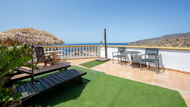 Eine Terrasse mit Meerblick, ein Reetdachschirm und Gartenmöbel.