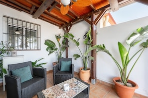 A patio area with wicker furniture, potted plants, and a tiled floor.
