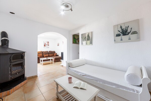 A living room with a white sofa, a small table with a book and a mug, a fireplace, and a wall with three potted plants.