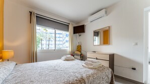 Hotellihuone, jossa on sänky, yöpöytä, peili, ikkuna verhoilla ja ilmastointilaite.