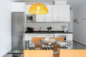 Una cocina moderna con armarios blancos, una mesa de comedor de vidrio y una lámpara colgante amarilla.