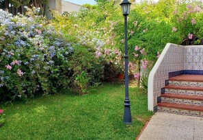 Un jardín con un farol, una escalera con baldosas estampadas y diversas plantas en flor.