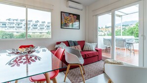 Un soggiorno moderno con un tavolo in vetro, sedie rosse e bianche, un divano rosso e un balcone con mobili da esterno.