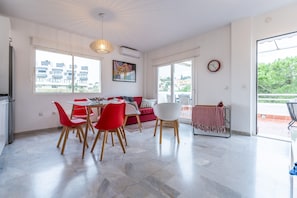Amplia sala de estar con una mesa de comedor, sillas rojas y blancas, un sofá rojo y un ventanal con vista a la ciudad.