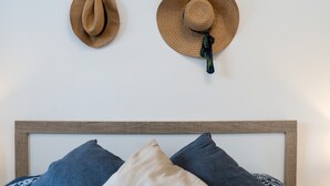 Due cappelli appesi a un muro, un letto con testiera in legno e un cuscino con motivo blu e bianco.