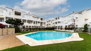 Una piscina circondata da un prato curato, con edifici bianchi sullo sfondo.