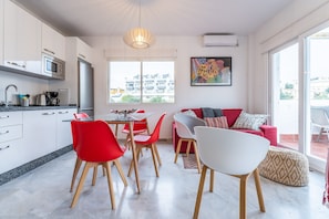 Una cocina moderna con comedor, un sofá rojo y blanco, y un ventanal con vista a edificios.