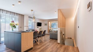 Cuina moderna amb una illa central, zona de menjador amb cadires i una escala que porta a un dormitori a l'àtic.