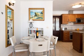 Un coin repas avec une table ronde, des chaises, un tableau, et une cuisine dotée de meubles en bois et d’appareils électroménagers.
