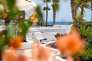 Un espace aménagé au bord de la piscine, avec des chaises longues, un palmier et une vue sur la mer.