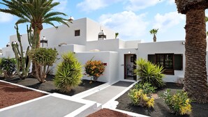 A white building with a flat roof, palm trees, and a garden with various plants. - Vacation Home 'Puerto Chico B' with Sea View, Shared Pool & Wi-Fi (Playa Blanca)