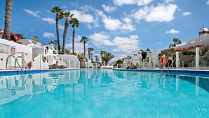A clear blue pool surrounded by palm trees and white buildings. - Vacation Home 'Puerto Chico B' with Sea View, Shared Pool & Wi-Fi (Playa Blanca)