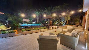 An outdoor patio area with wicker furniture, a pool, and palm trees. - Villa 'Tore' with Sea View, Wi-Fi, and Air Conditioning (Quartu Sant'Elena)