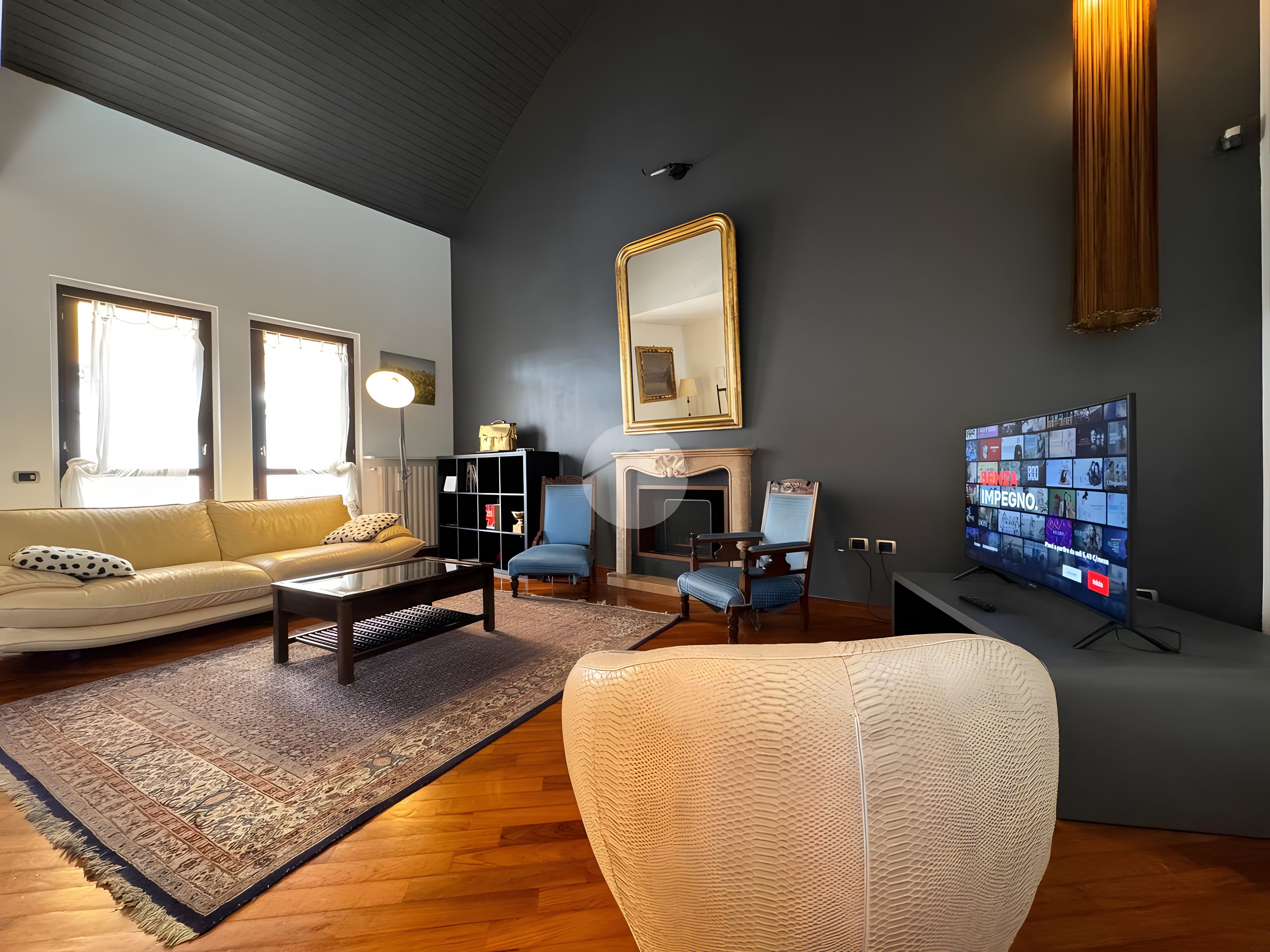 A modern living room with a sofa, armchairs, a coffee table, a fireplace, a television, and a bookshelf.