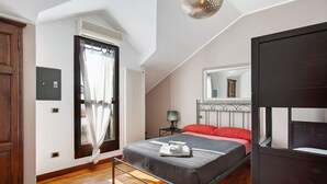 A bedroom with a bed, a window with curtains, a bedside table with a lamp, and a mirror on the wall. - "Villa La Palmetta" with Pool, Terrace & Wi-Fi (Peschiera Borromeo)