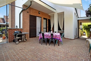 Un patio con mesa y sillas, una parrilla y un muro de ladrillo.
