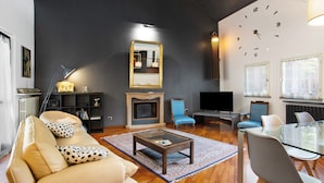 A living room with a sofa, coffee table, TV, fireplace, and a clock on the wall. - "Villa La Palmetta" with Pool, Terrace & Wi-Fi (Peschiera Borromeo)