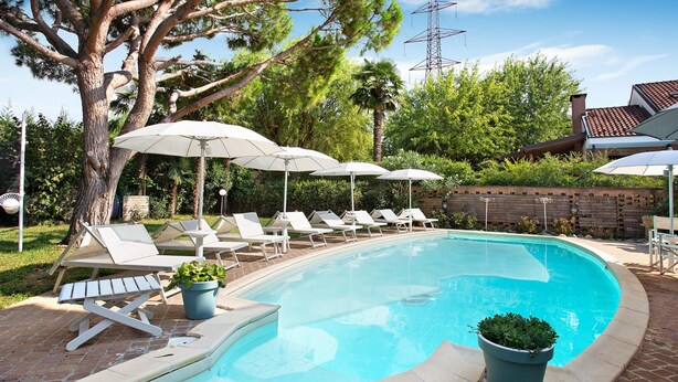 A swimming pool with lounge chairs and umbrellas, surrounded by greenery and a brick wall. - "Villa La Palmetta" with Pool, Terrace & Wi-Fi (Peschiera Borromeo)