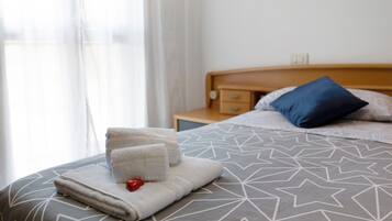 Een net opgemaakt bed met een sprei met een geometrisch patroon, een blauw kussen en een nachtkastje met een lamp.
