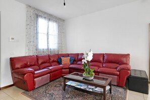 Ein rotes Ledersofa, ein Glastisch mit Zeitschriften, ein gemustertes Teppich und ein Fenster mit durchsichtigen Vorhängen.