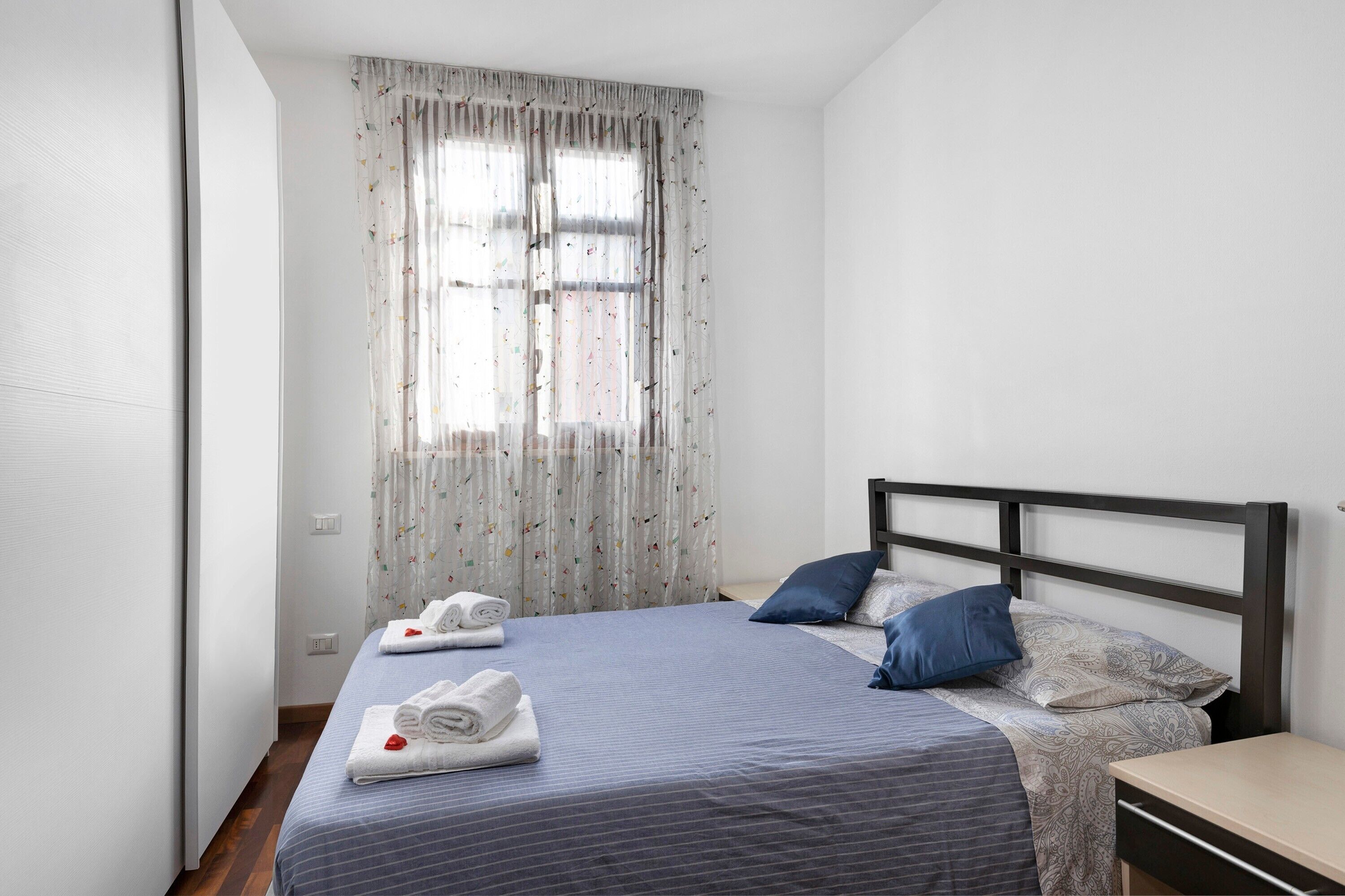 Un lit simple avec une tête de lit, une table de chevet et une fenêtre avec des rideaux.