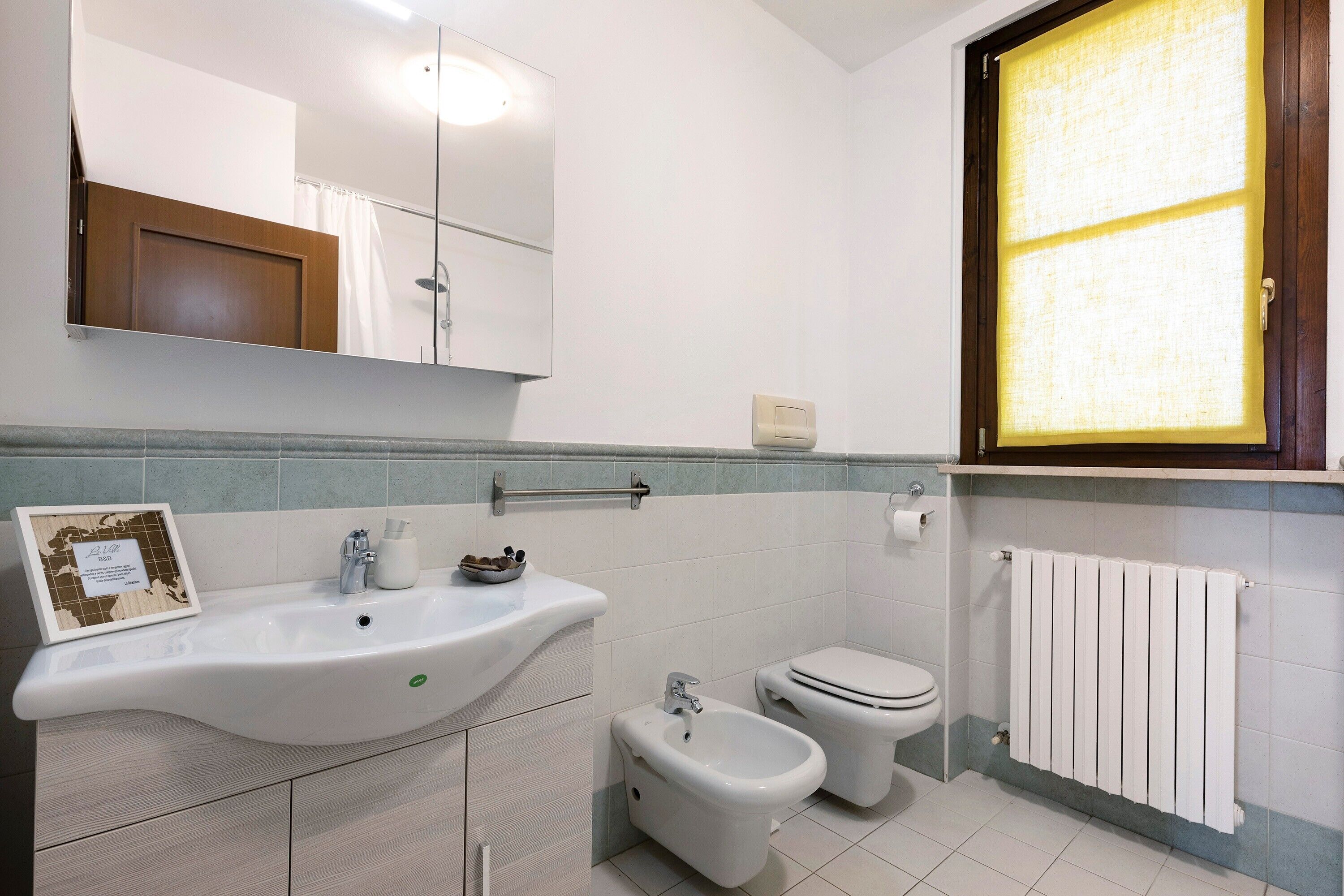 Un baño con lavamanos, bidé, inodoro y ventana con persianas.