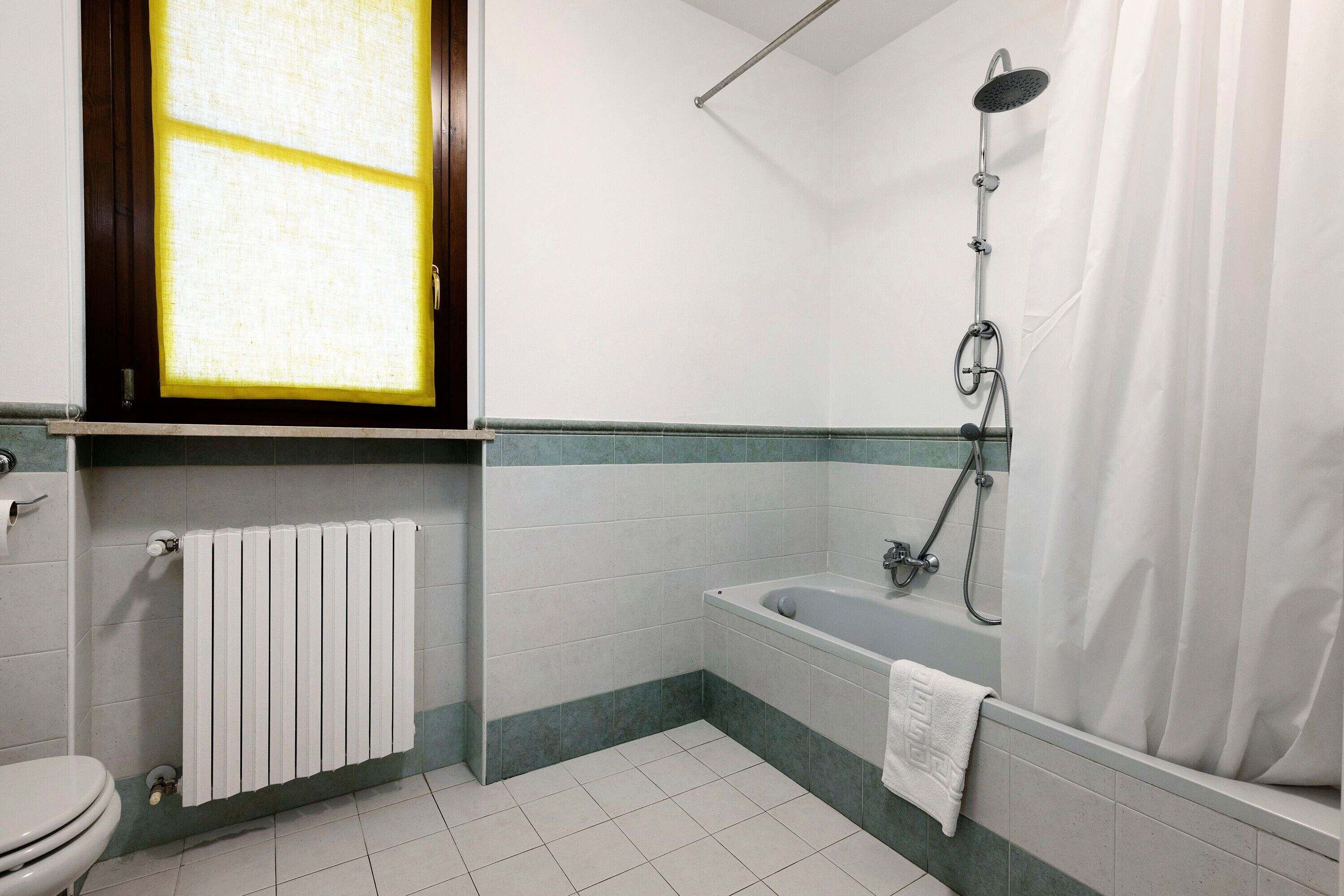 A bathroom with a toilet, a bathtub, a shower, a window, and a radiator.