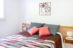 A bed with a quilt, two pillows, a bedside table with a lamp, and a wall art piece.