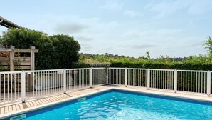 Ein rechteckiger Swimmingpool mit einer gefliesten Kante, umgeben von einem weißen Metallzaun und einer Holzterrasse.