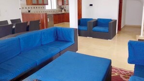 Una sala de estar moderna con sofás azules, una zona de comedor con una mesa y sillas, y una cocina al fondo.
