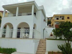 A white two-story building with a balcony, arched windows, and a staircase leading to the entrance. - Maison Charmante - vue 360° mer et Montagnes (Tabarka)