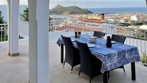 Un área de comedor al aire libre techada con una mesa dispuesta para dos, con vistas a una ciudad costera.