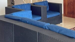 Una sala moderna con una escalera, muebles de mimbre oscuro y una puerta de madera.