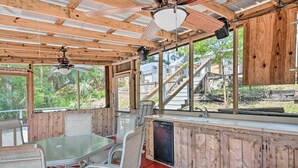 A covered outdoor dining area with a glass table and chairs, wooden walls, and a view of a staircase and greenery. - Peaceful Satsuma Escape w/ Dunns Creek Access (Satsuma)