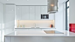 A modern kitchen with white cabinetry, a stainless steel microwave, and a large island with stools. - Av. Liberdade 4 - Duque de Palmela (Lisbon)