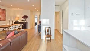 A modern living room with a brown leather sofa, a dining area with white chairs, a wooden chair, and a white kitchen area. - Av. Liberdade 4 - Duque de Palmela (Lisbon)