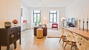 A modern living room with a sofa, a dining table with chairs, a small side table, a lamp, and a television. - Av. Liberdade 4 - Duque de Palmela (Lisbon)