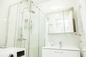 A modern bathroom with a glass shower enclosure, a white sink with a mirror, and a white cabinet.