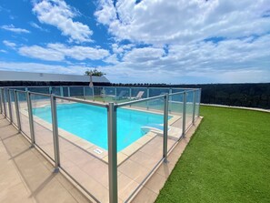 Ein klarer, blauer Pool mit Glasumrandung, umgeben von einem gepflegten Rasen und einer Steinmauer.