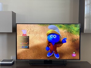 Televisiossa näkyy sarjakuvahahmo, ja sen edessä olevalla pöydällä on kaukosäädin ja älypuhelin.