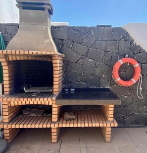 A brick-built outdoor oven with a chimney, a stone wall, and a lifebuoy hanging on the wall.