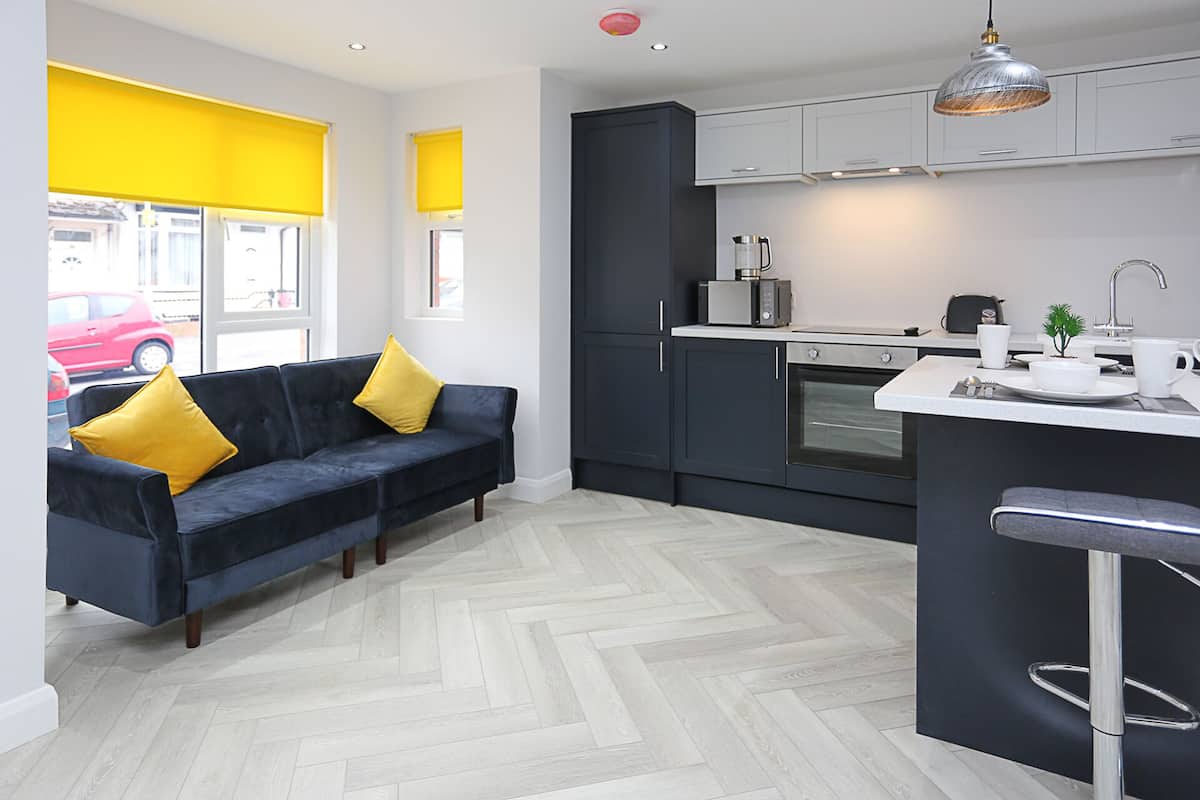 A modern kitchen with dark cabinets, a herringbone-patterned floor, a bar area, and a sofa with yellow cushions.