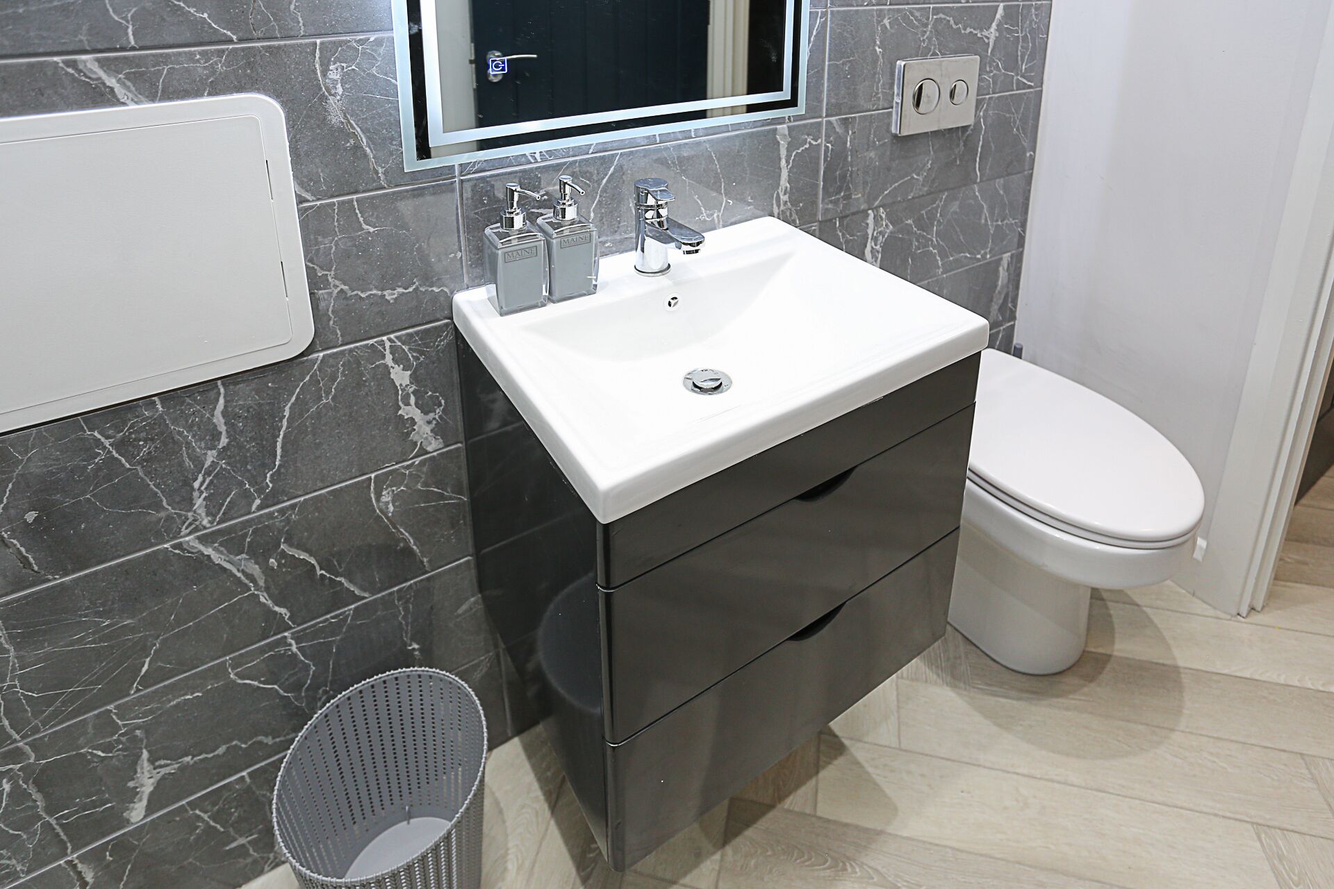 A bathroom with a white sink, dark marble walls, and a toilet.