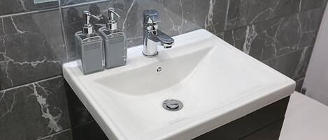 Et badeværelse med en hvid vask, to sæbedispensere, et spejl over vasken og et toilet.