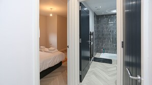 Een moderne hotelkamer met een bed, een badkamer met een marmeren douche en een visgraatvloer.
